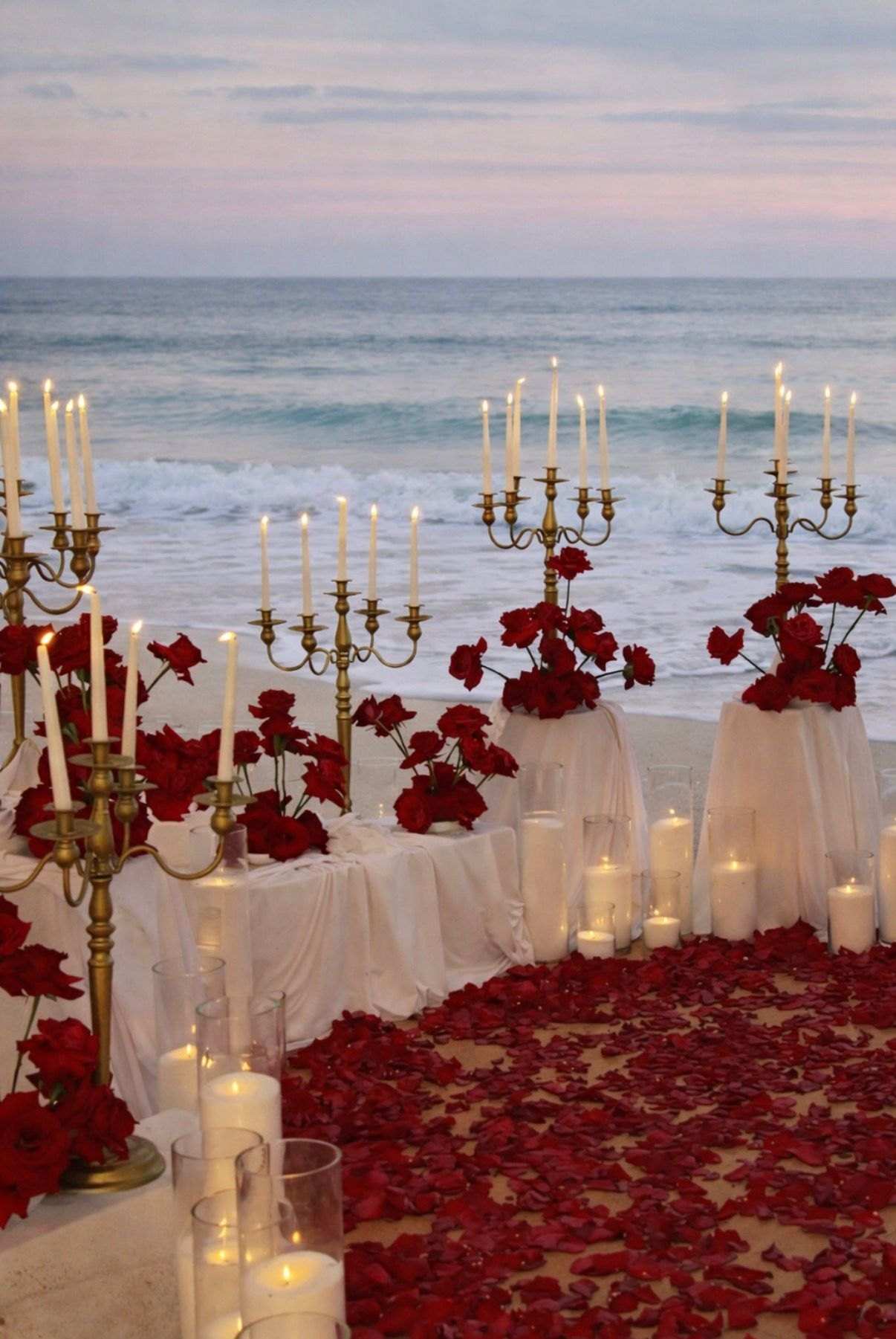 Red roses, gold candelabras and draped pedestals with candles on the beach