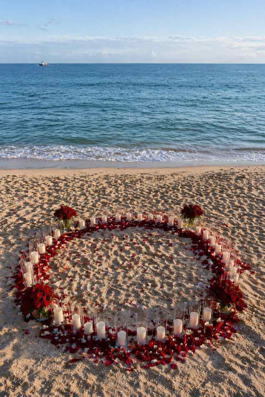 Circle of candles and red rose petals on the sand by the ocean