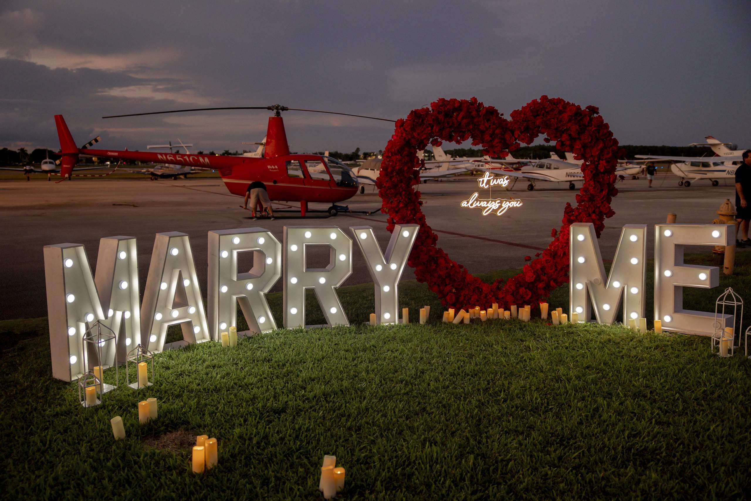 Helicopter beside illuminated Marry Me letters on an airfield