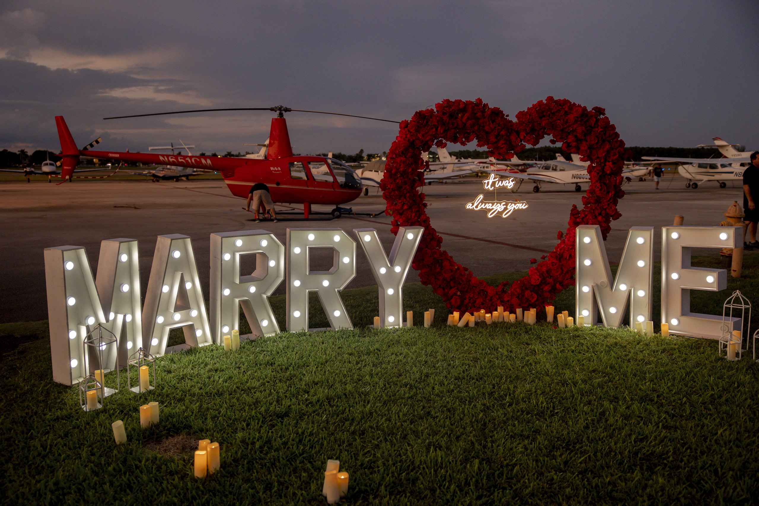 Helicopter beside illuminated Marry Me letters on an airfield