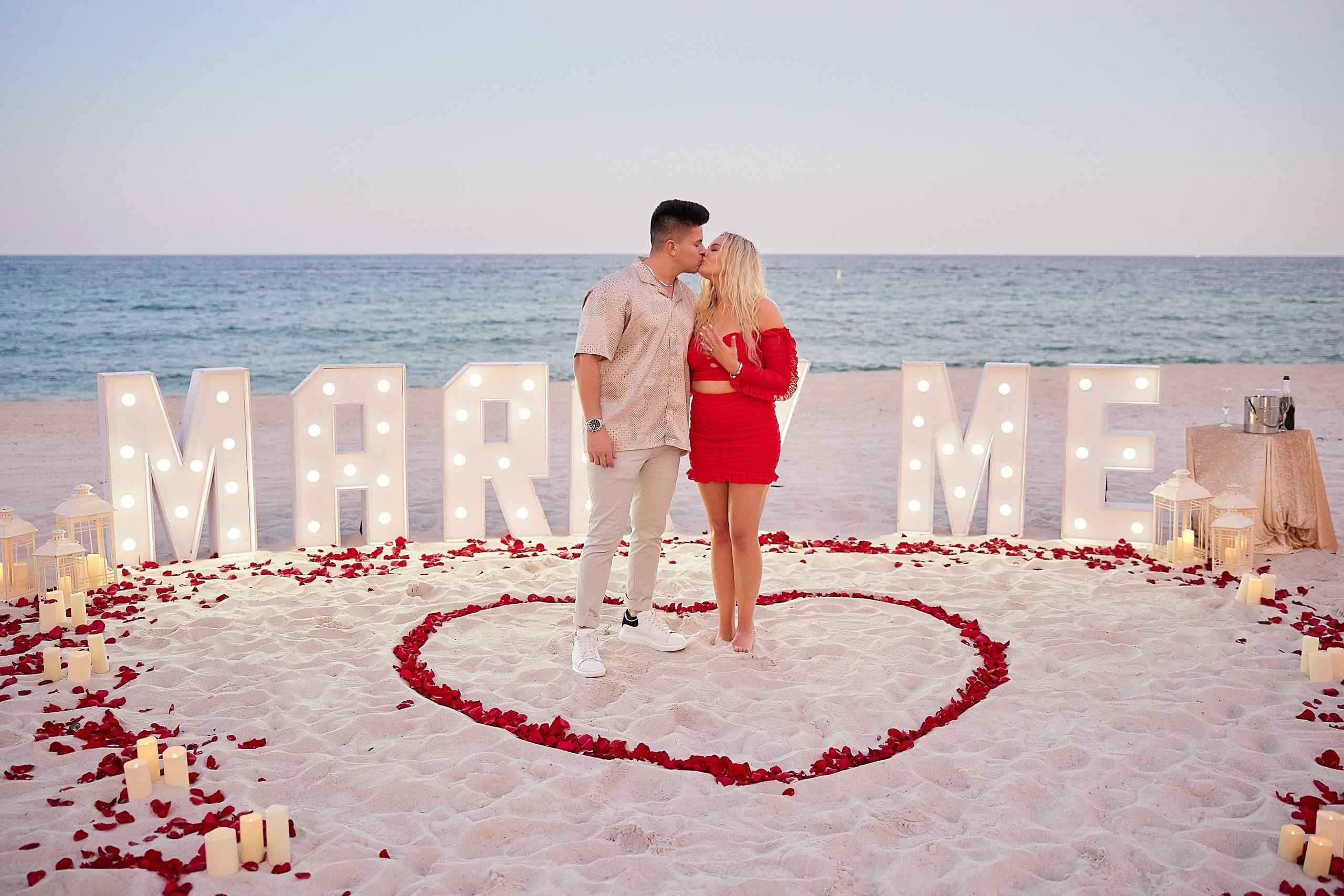 Couple in front of illuminated Marry Me letters and red roses