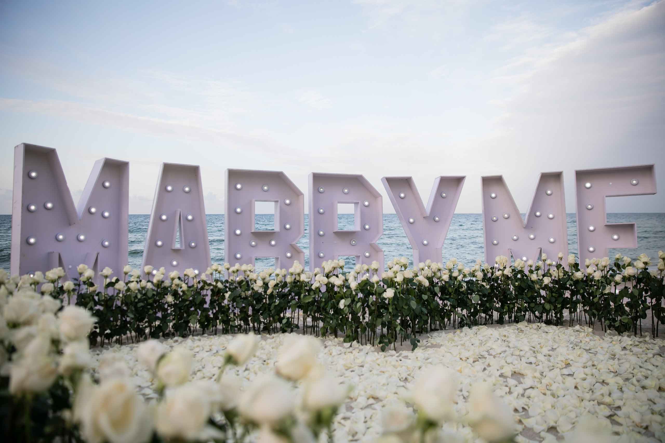 Large Marry Me letters framed by white roses and candelabras