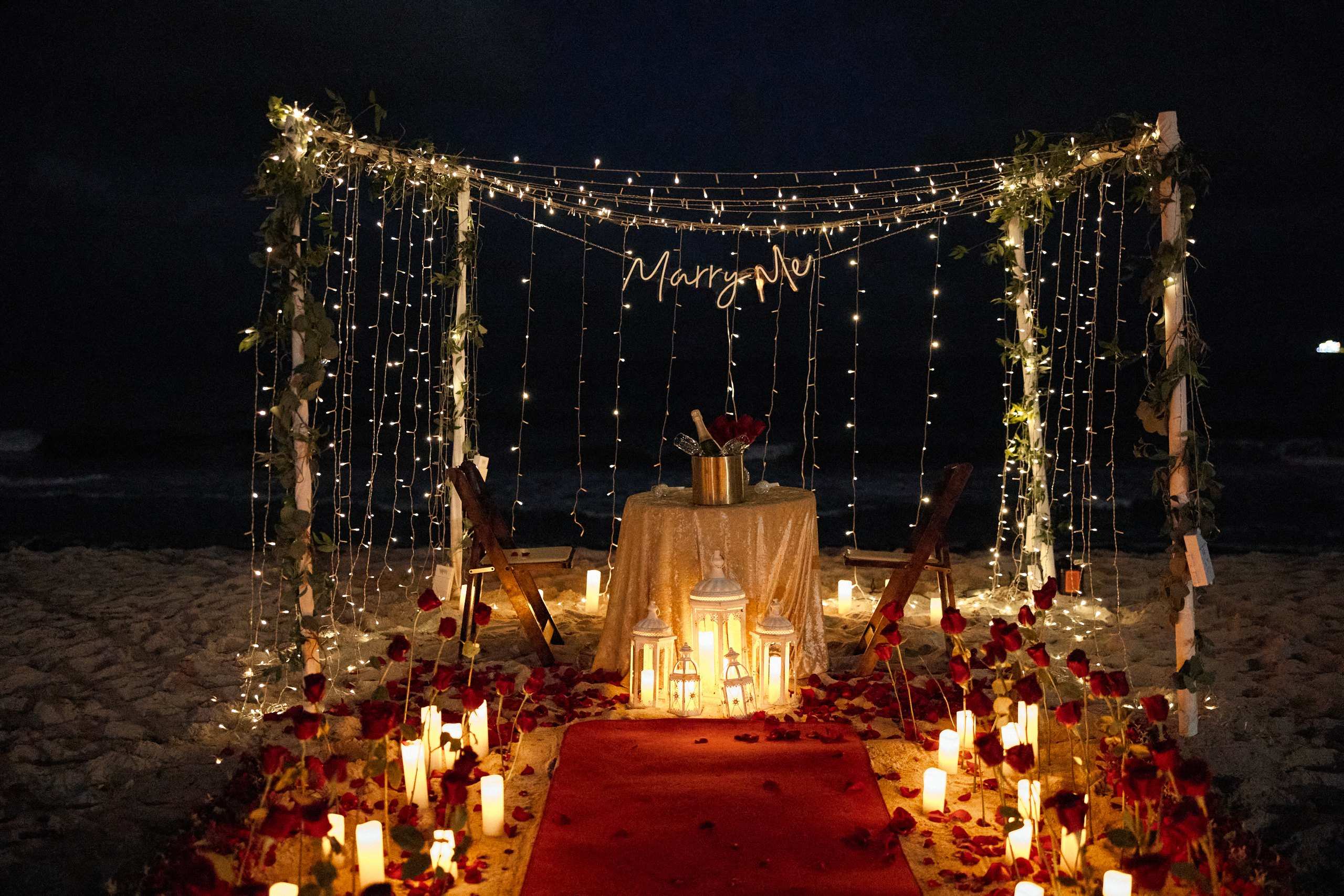 Candlelit dinner table under a draped canopy on the beach at night