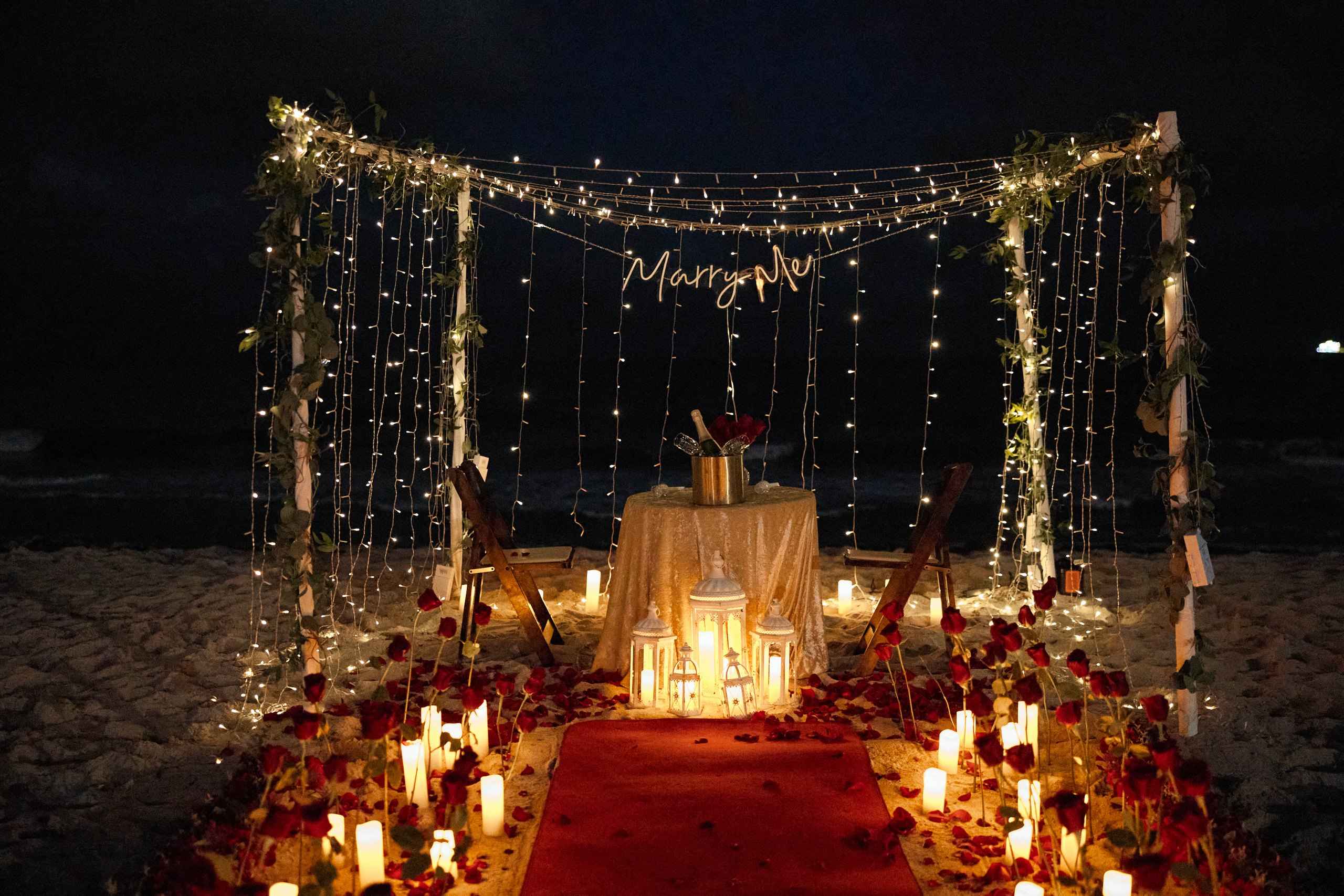 Candlelit dinner table under a draped canopy on the beach at night