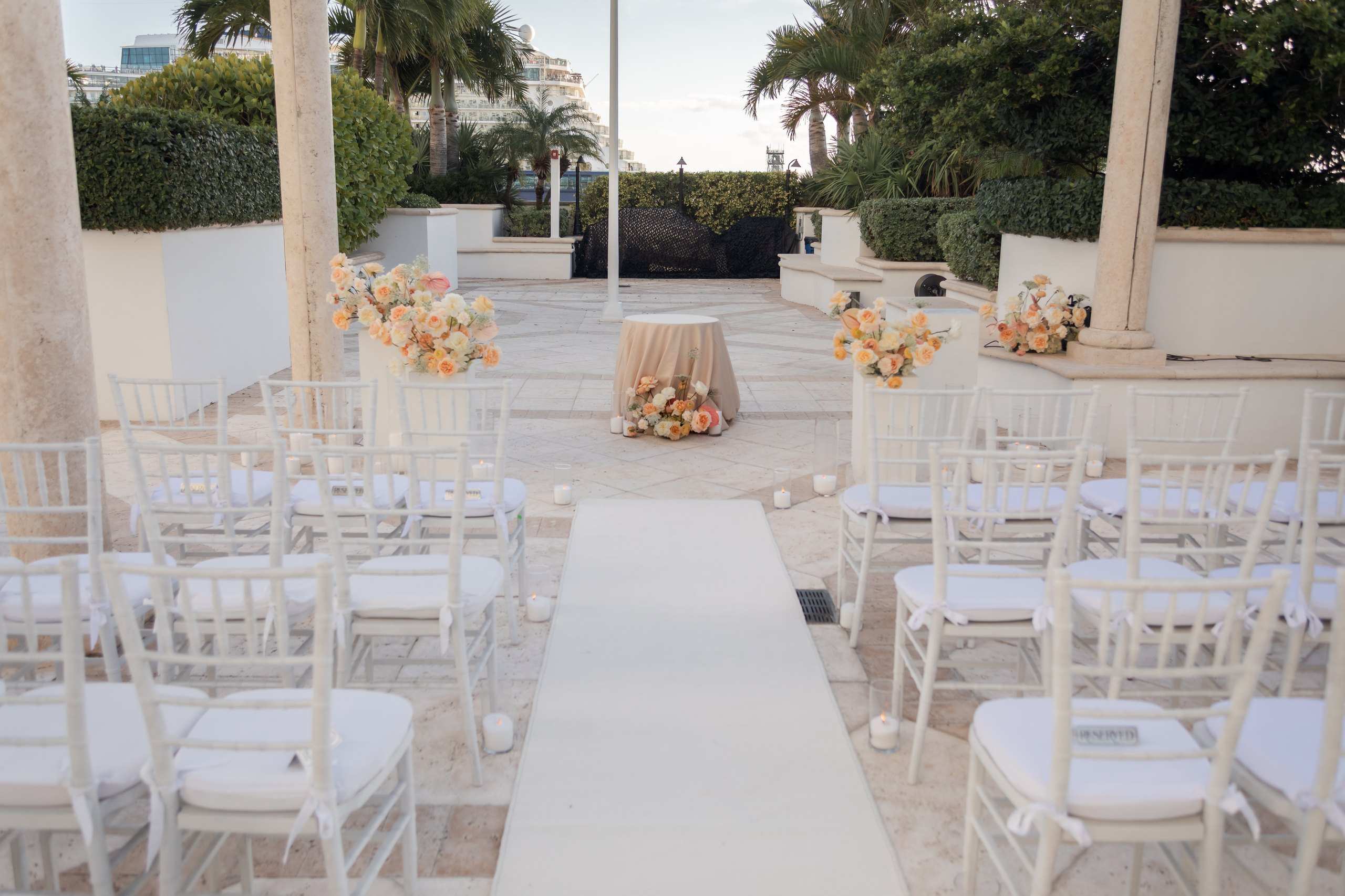 White pedestals with flowers lining an aisle under a pergola