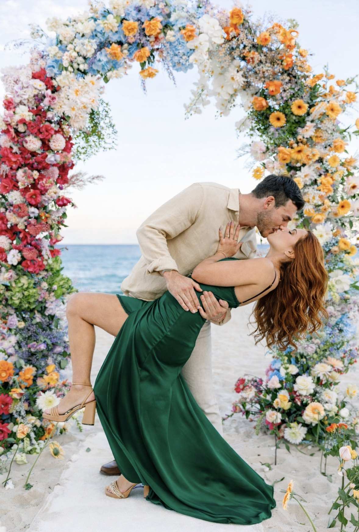 Couple kissing under a colorful floral arch on the beach